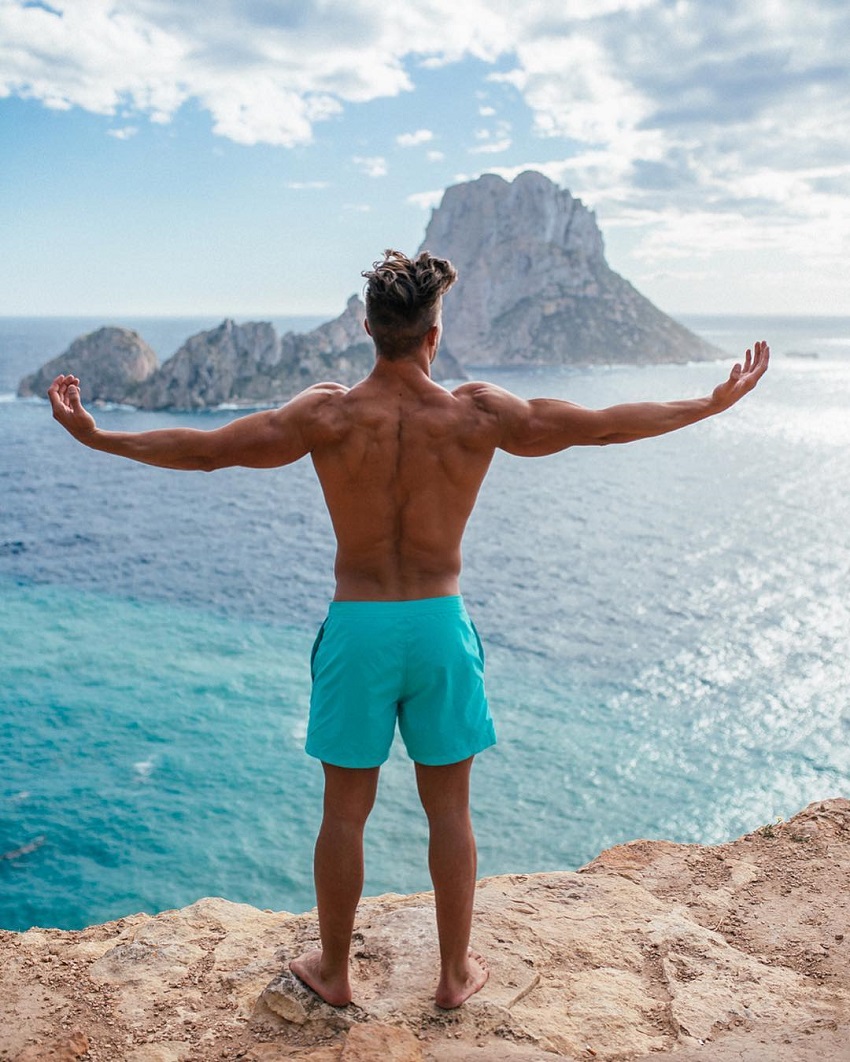 Antonio Pozo standing on a cliff overlooking a vast blue sea with his arms raised in the air