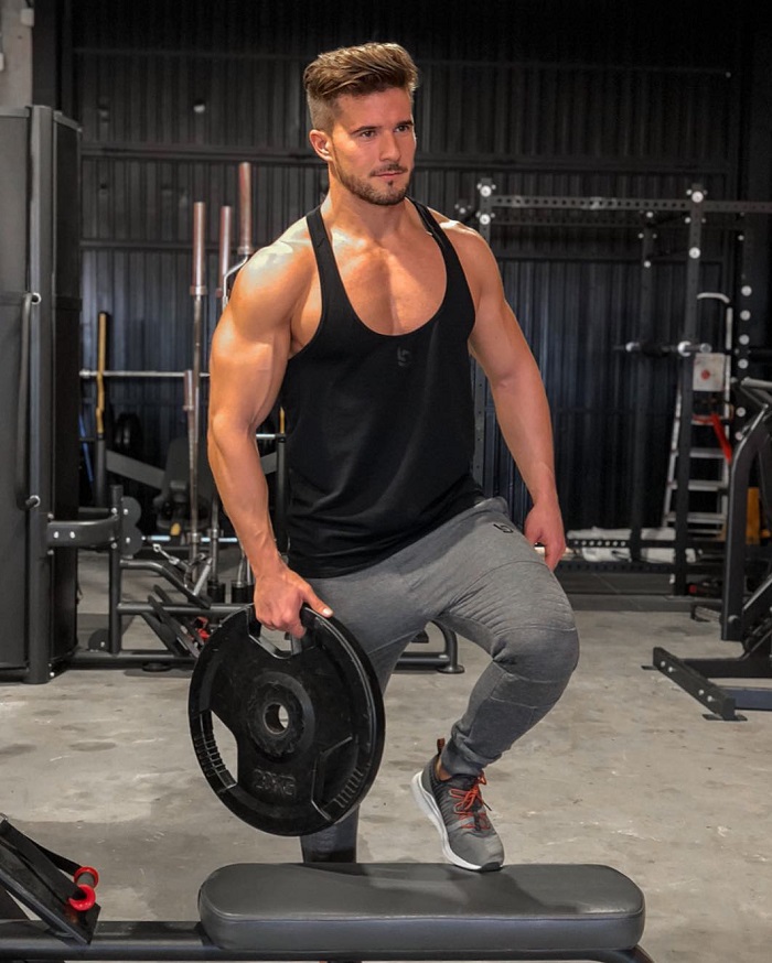 Antonio Pozo standing in the gym holding a weight plate looking fit