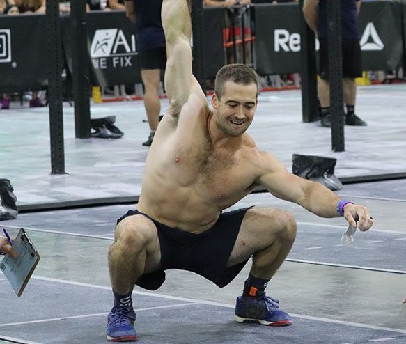 Ben Smith doing an overhead press with a dumbbell during a CrossFit event