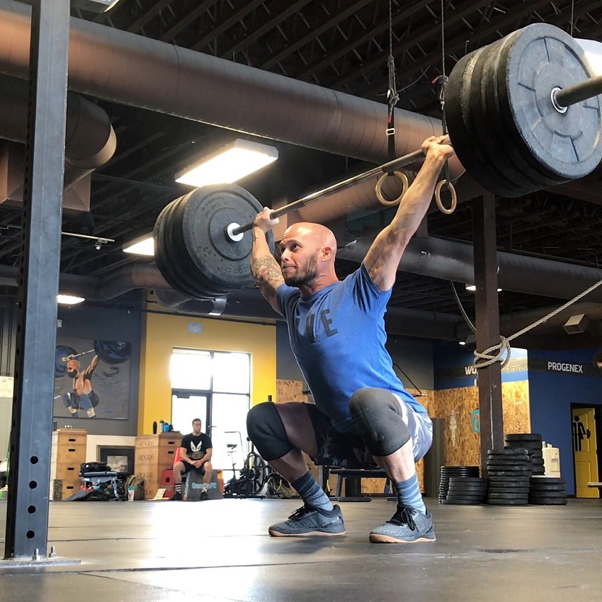 Chris Spealler doing an overhead press with barbells looking strong and fit