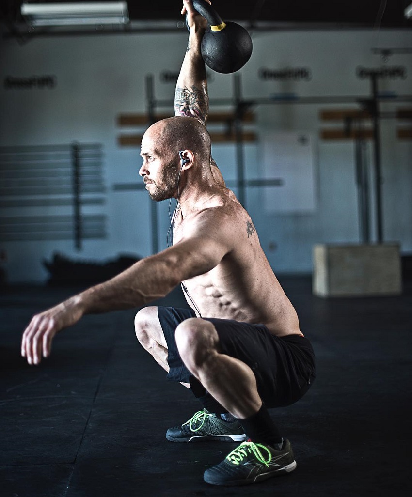 Chris Spealler doing a squatting overhead kettlebell press looking ripped