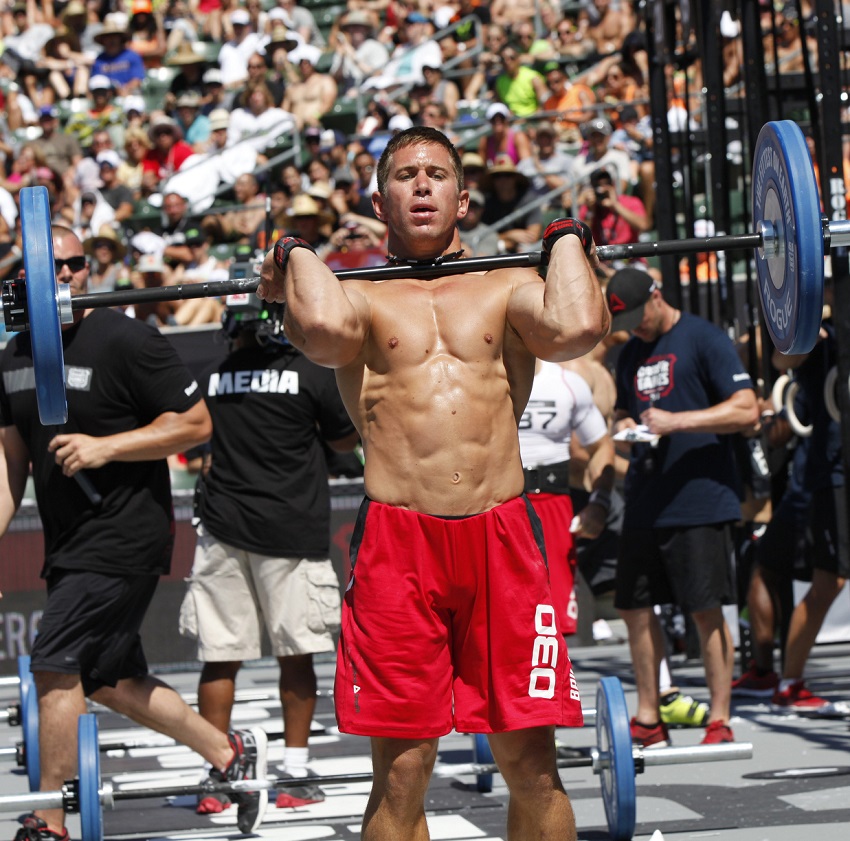 Dan Bailey lifting a heavy overhead press while being shirtless during a CrossFit competition