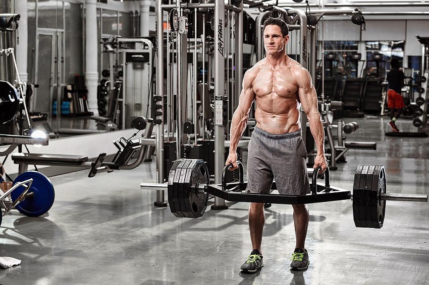 Don Saladino performing a heavy compound exercise in the gym while shirtless