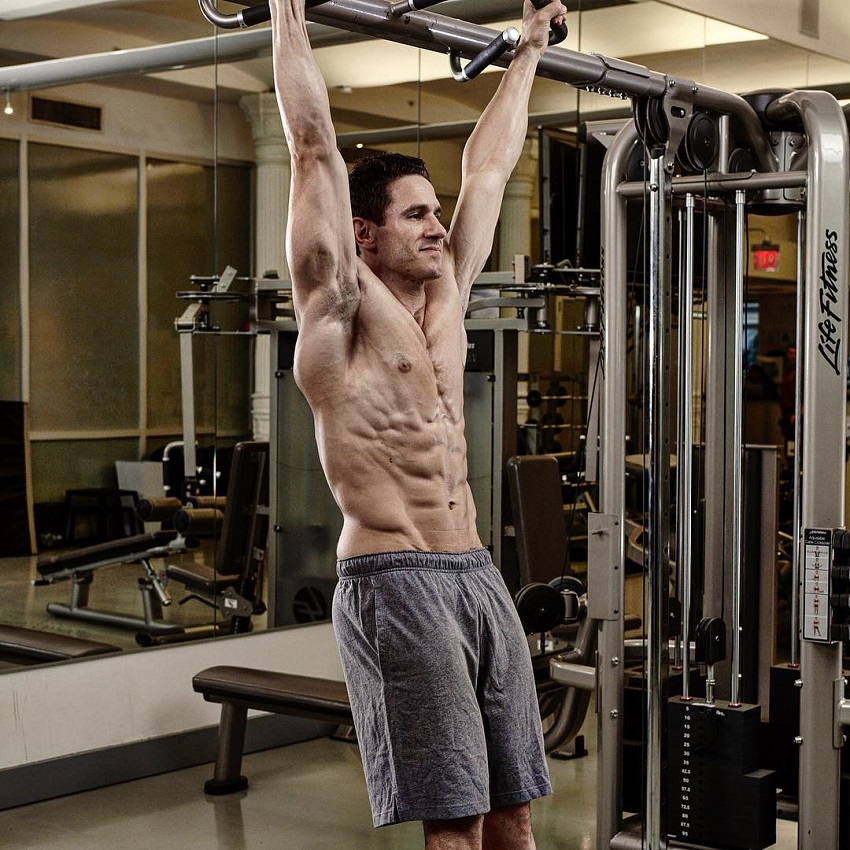 Don Saladino hanging on a pull up bar looking ripped without a shirt on