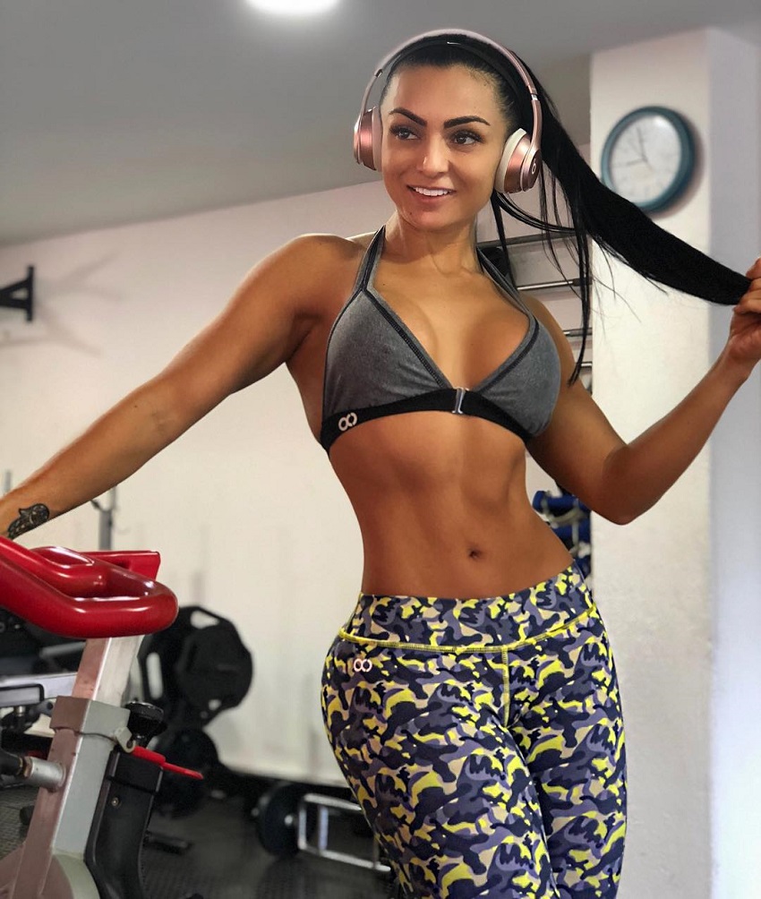 Paola Macias psoing for a photo in a gym wearing headphones looking fit and lean