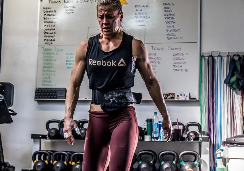 Rebecca Voigt Miller in a CrossFit gym with kettlebells behind her back, looking exhausted from training