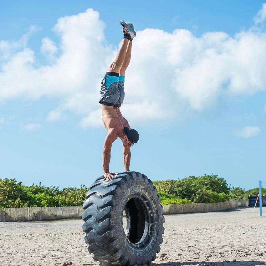 Shawn Ramirez doing a handstand on a big tire on the beach