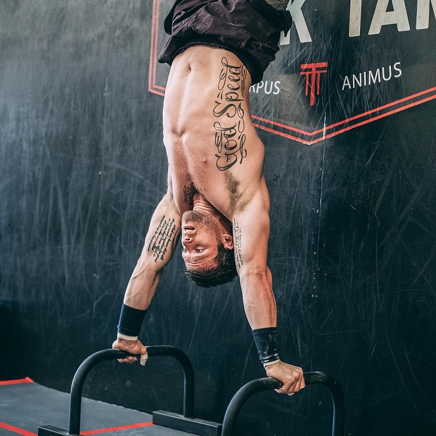 Travis Mayer doing a hand stand on bars looking fit and lean