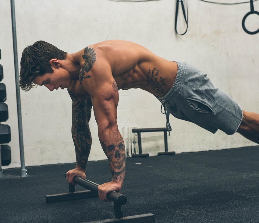 Adi Gillespie doing push ups in a gym while shirtless, showcasing his bulging triceps