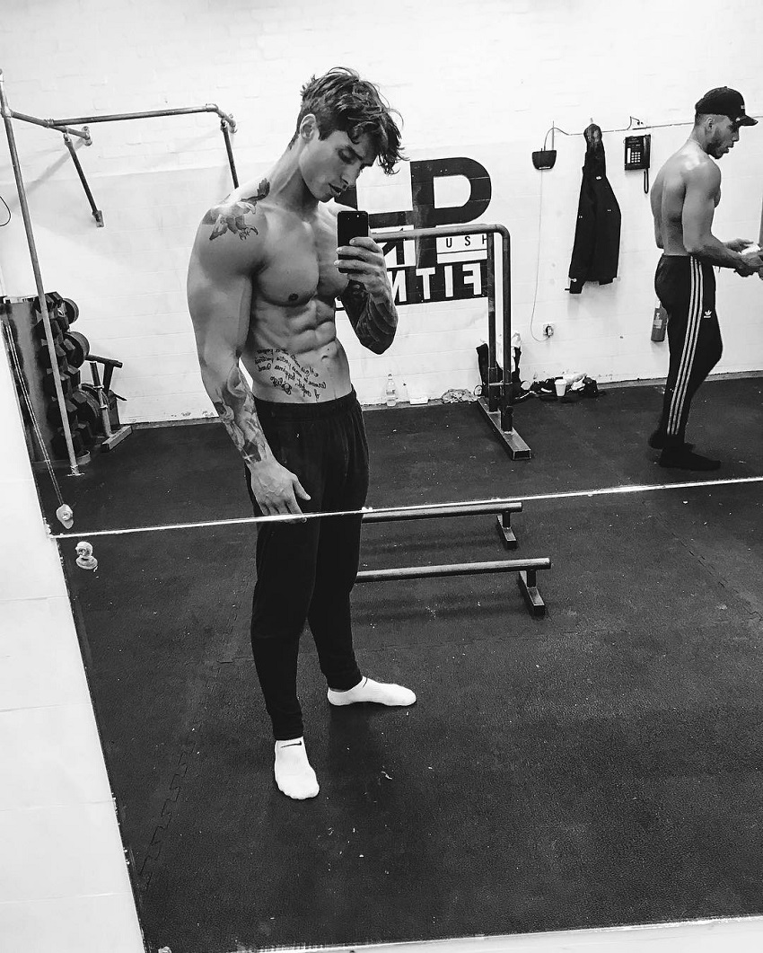 Adi Gillespie taking a picture of his shirtless body in a gym looking fit