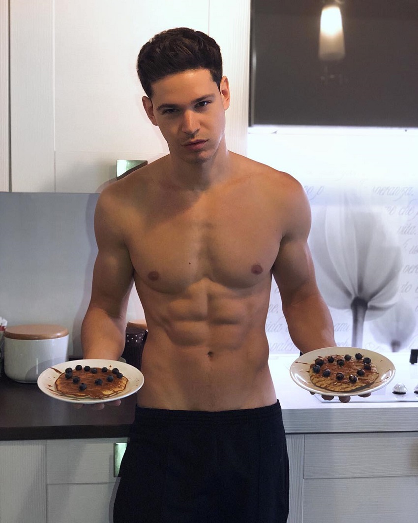 Andrea Moscon posing shirtless with two plates in his hands looking ripped