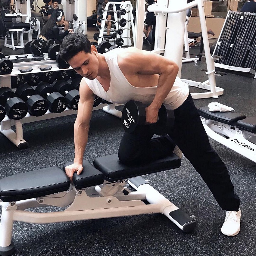 Andrea Moscon training in the gym with a dumbbell, wearing a white tank top