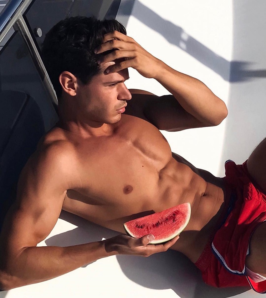 Andrea Moscon lying shirtless on a boat with a watermelon in his hand, looking ripped