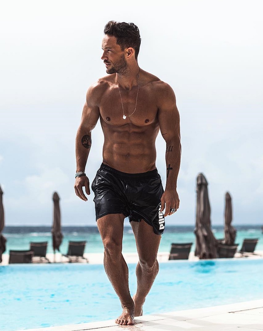 Daniel Fox walking on a beach looking ripped and strong