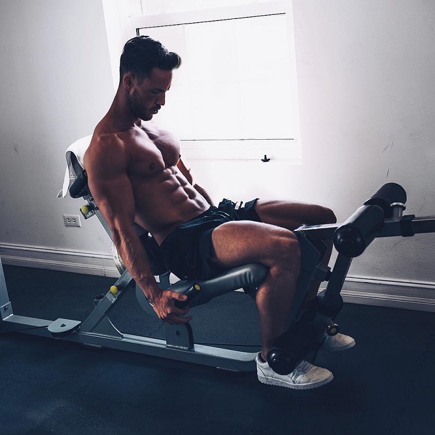 Daniel Fox doing a seated leg exercise while shirtless, looking ripped