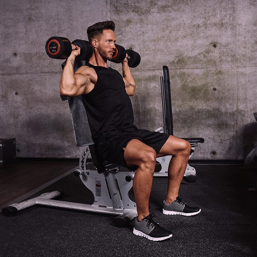 Daniel Fox doing a seated overhead dumbbell press in a gym