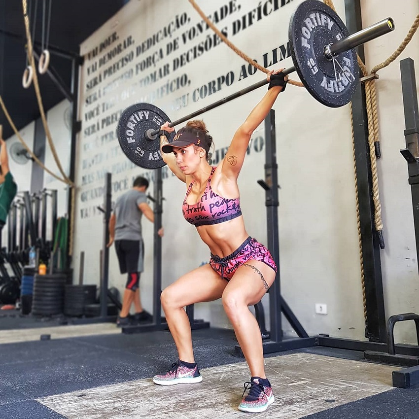 Natalia Carvalho doing an overhead barbell press looking strong