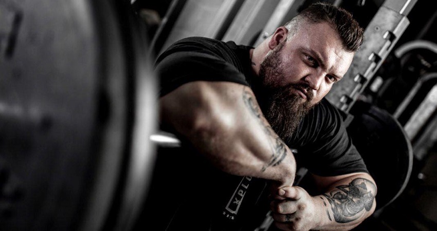 Eddie Hall posing for the camera leaning against a barbell loaded with weights