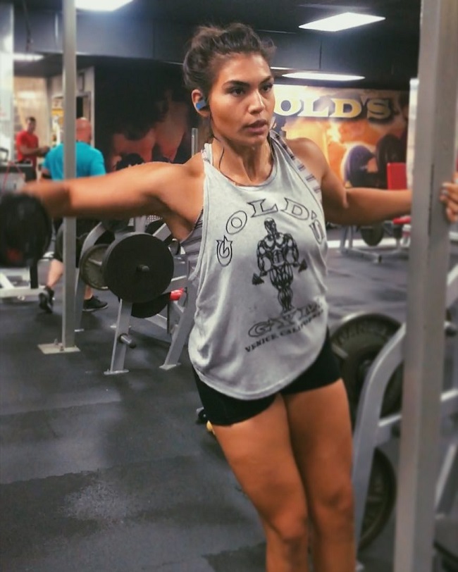 Laura Micetich doing dumbbell lateral raises in the gym