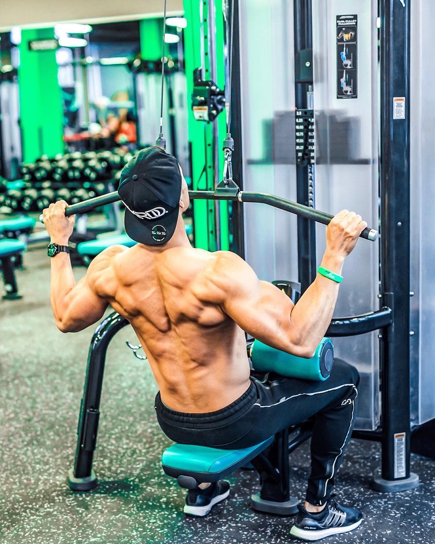 Nam Vo performing lat pulldowns shirtless, looking muscular and ripped