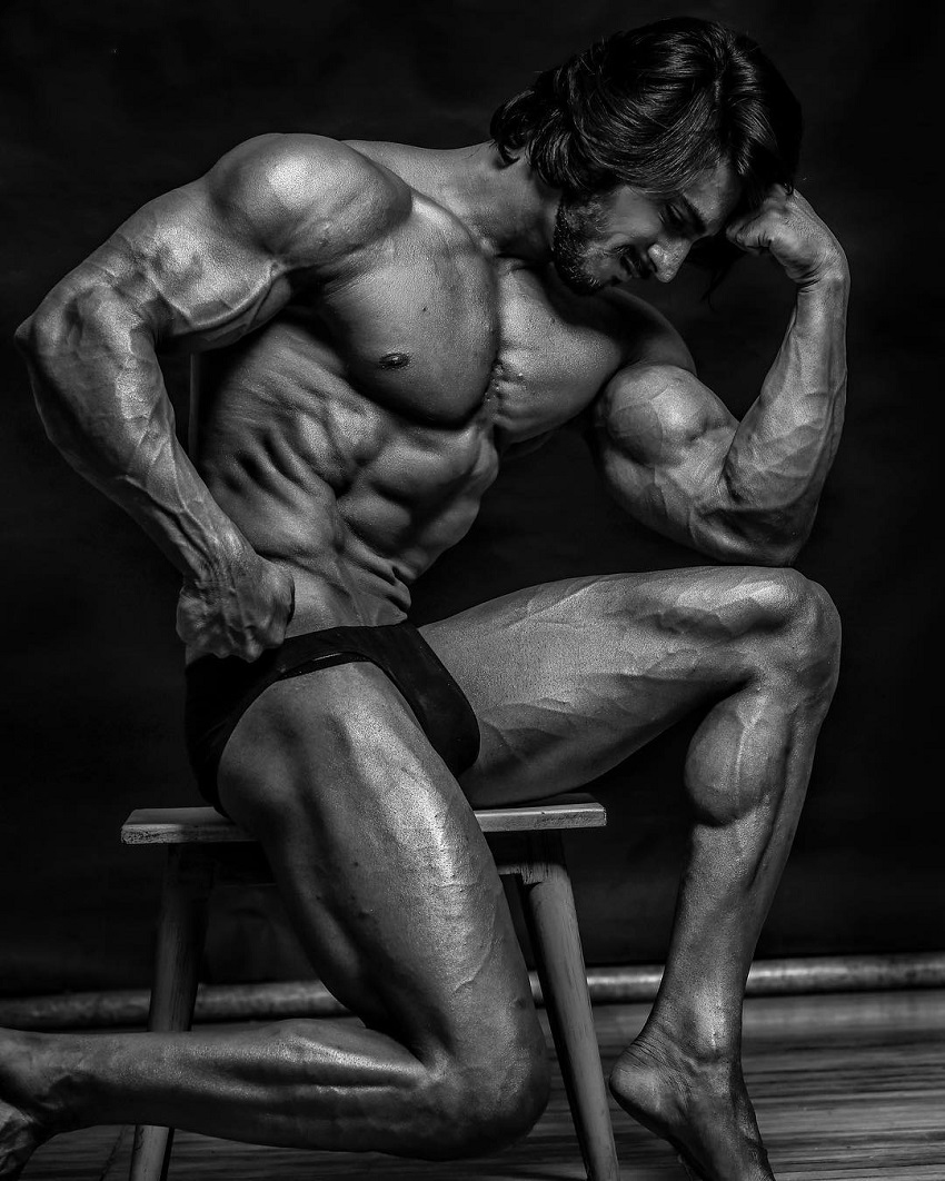 Thakur Anoop Singh sitting shirtless on a chair looking extremely ripped from the side