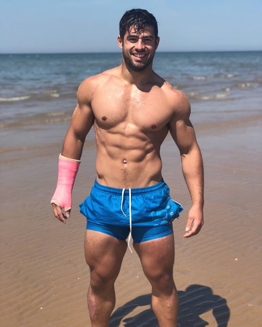 Dan Tai posing shirtless on the beach looking fit and lean