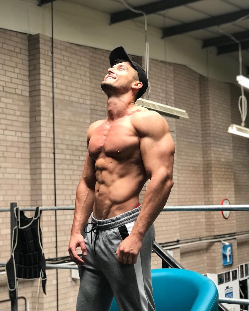 Josh Watson standing shirtless in a gym looking up in the ceiling and laughing