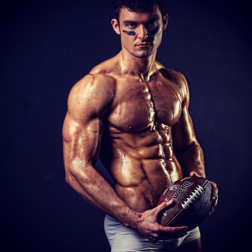 Josh Watson posing shirtless with a rugby ball, looking muscular and ripped