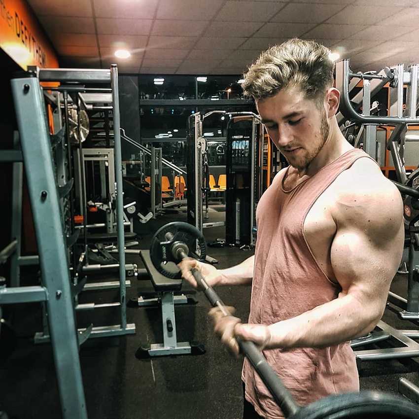 Matt Lucas doing barbell biceps curls in a gym