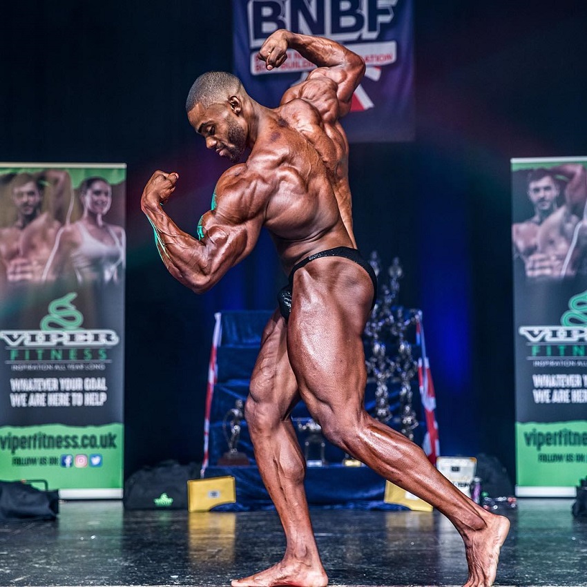 Nathan Williams flexing his arms and back on the bodybuilding stage