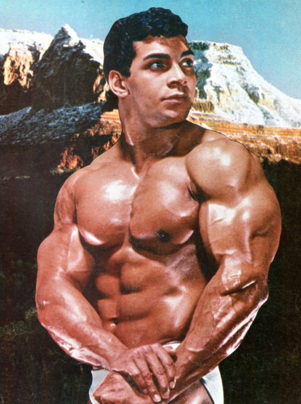 Harold Poole flexing shirtless with a mountain in the background