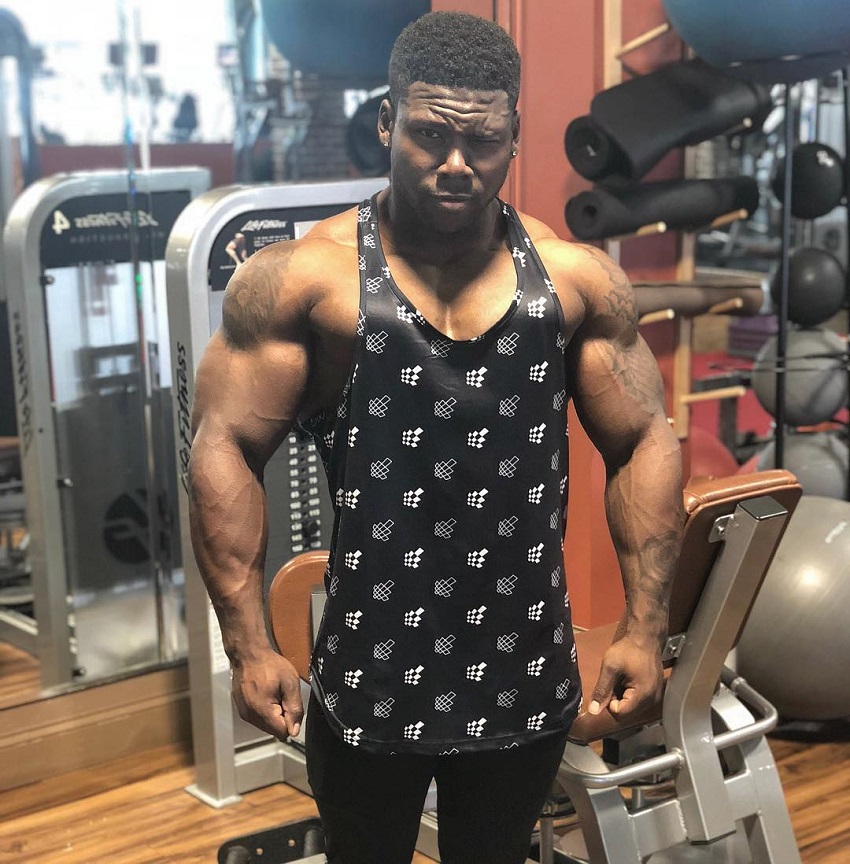 Keone Pearson standing in a black tank top with white spots, looking strong and ripped