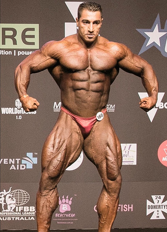 Rouhollah Mirhoseini standing on the bodybuilding stage looking riped