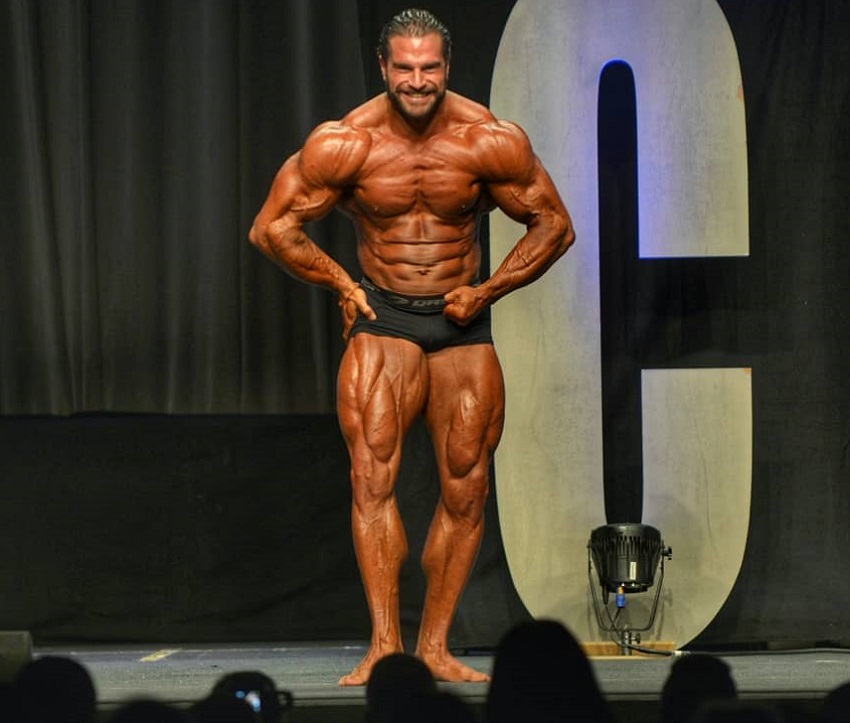 David Hoffmann posing on the bodybuilding stage showing off his swole and ripped muscles