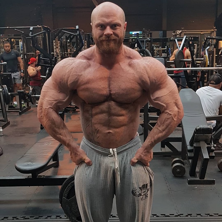 James Hollingshead flexing shirtless in a gym looking vascular, ripped, and huge