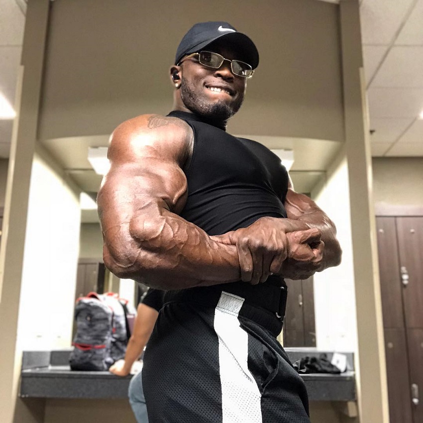 Kenneth Owens doing a side chest pose in a gym locker room