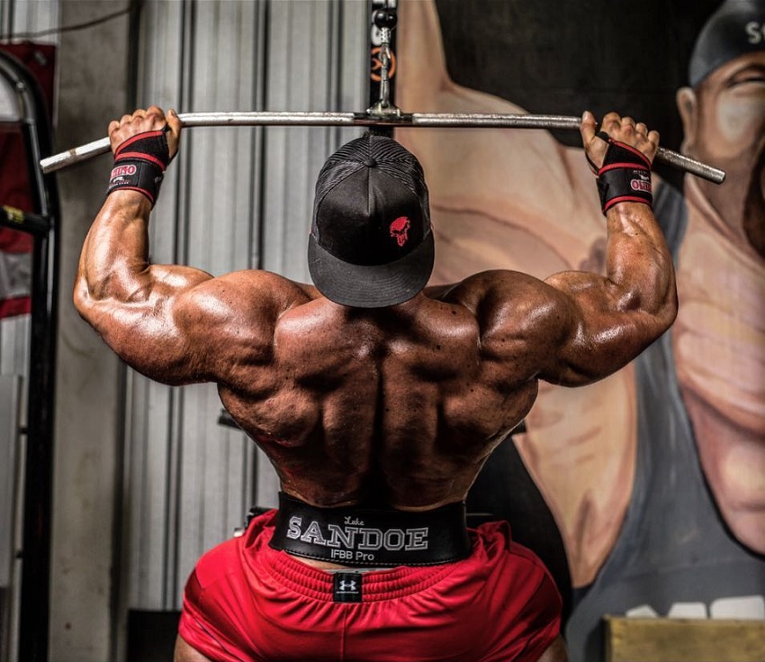 Luke Sandoe doing lat pulldowns while shirtless, looking huge and ripped