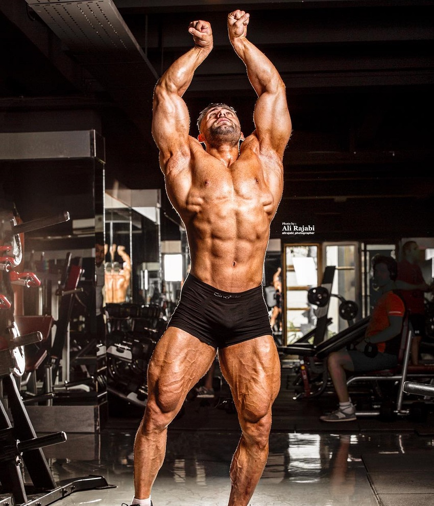 Ahmad Parvin posing shirtless in a gym photo shoot looking swole and ripped