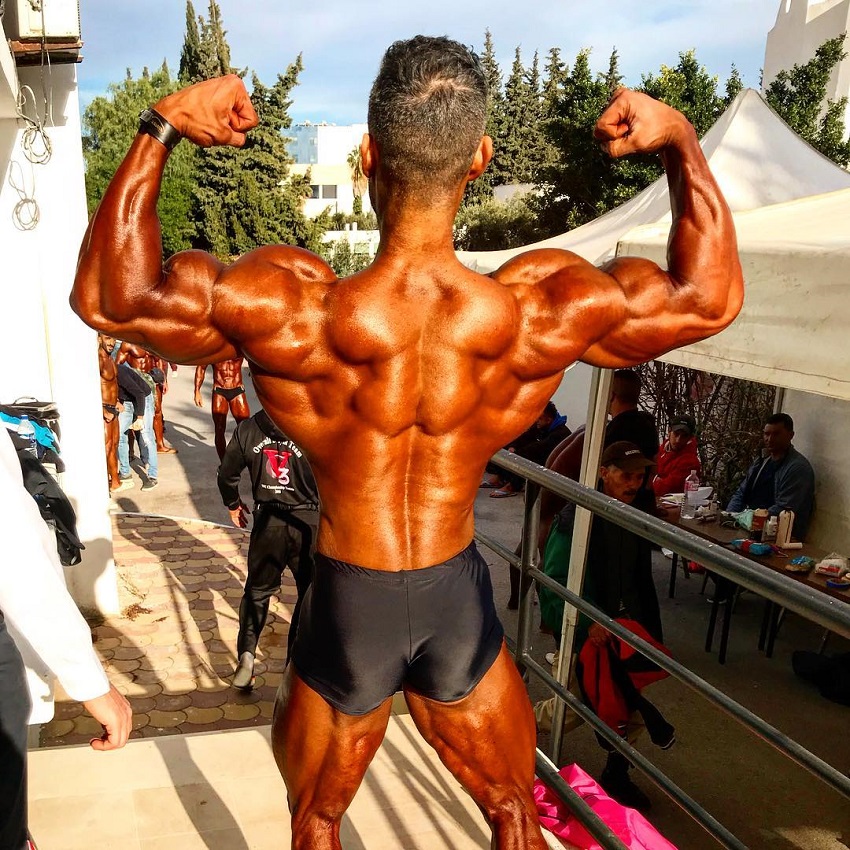 Ahmad Parvin doing a back double biceps outdoors in the contest warm-up area