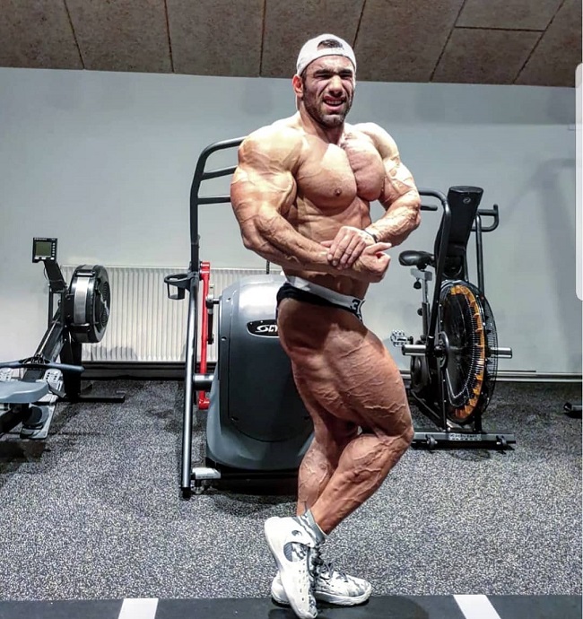 Ayat Bagheri doing a side chest pose for the photo looking ripped and big