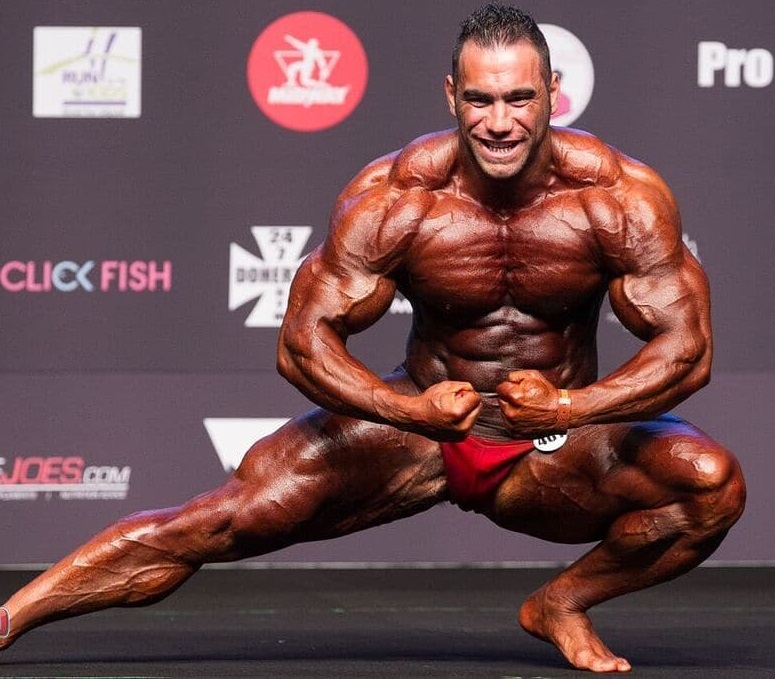 Ayat Bagheri performing a posedown on a bodybuilding stage looking swole and ripped