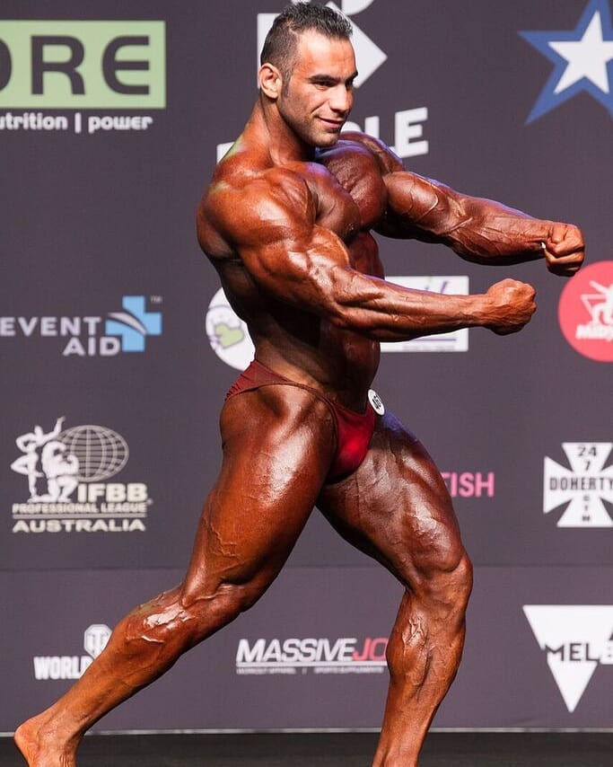 Ayat Bagheri showing his flexed arms from the side on the bodybuilding stages