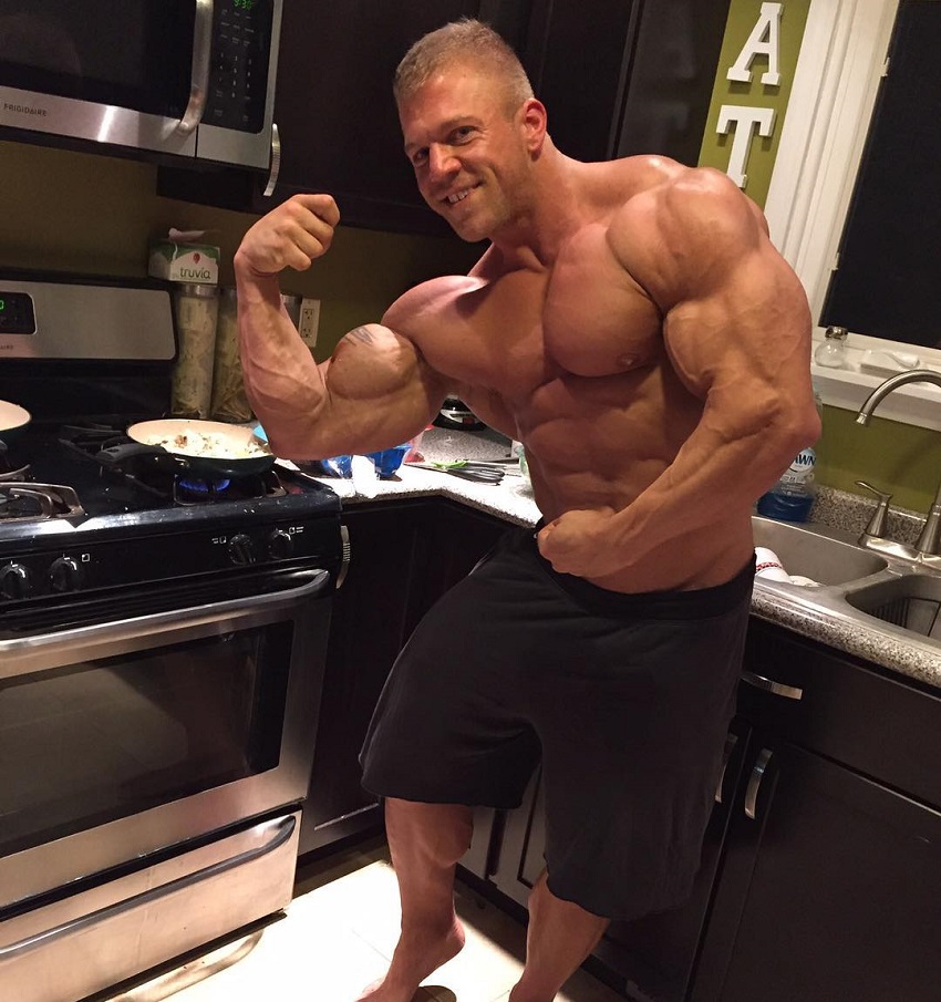 Brandon Beckrich flexing his biceps while being shirtless in the kitchen