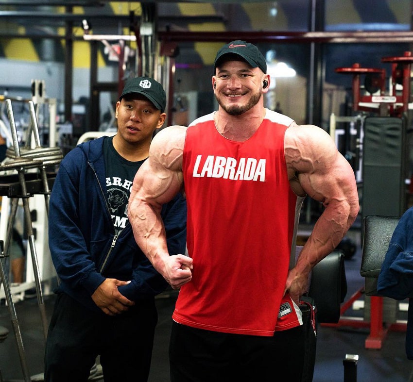 Hunter Labrada flexing for the photo in a red tank top looking massive