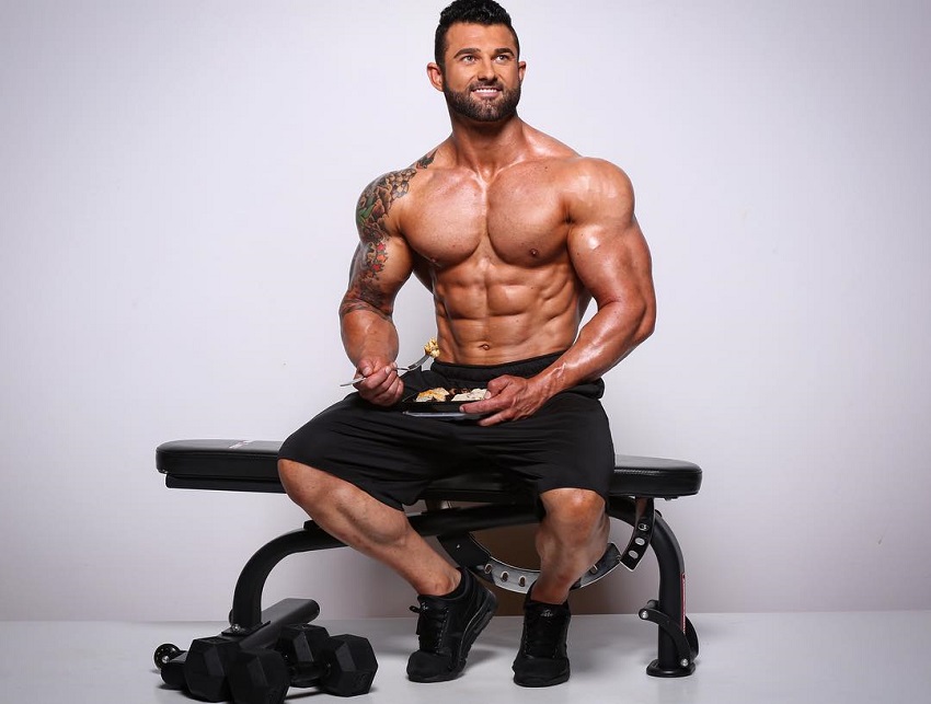 Jase Stevens sitting shirtless on a bench with food in a tupperware