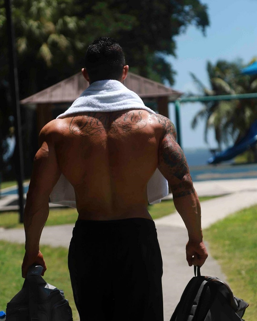 Jase Stevens walking shirtless down the road carrying bags, looking swole and ripped