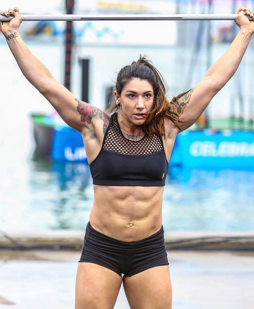 Kat Leone lifting heavy barbell overhead during a crossfit contest