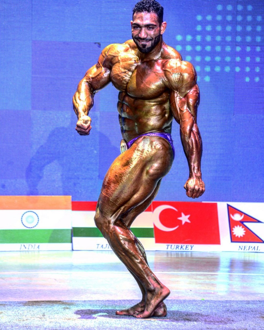 Yasin Qaderi doing a side tricep flex in front of a judges in a bodybuilding contest