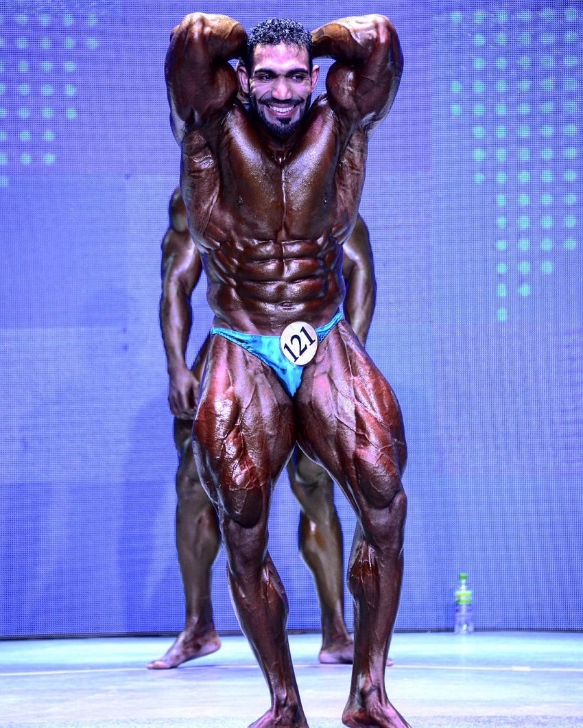 Yasin Qaderi flexing abs on a bodybuilding stage