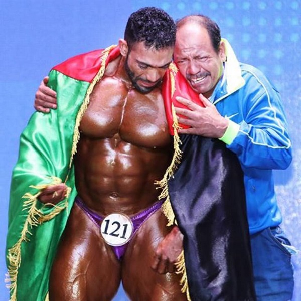 Yasin Qaderi crying with his coach on a stage after being proclaimed the victor, carrying Afghan flag on his body